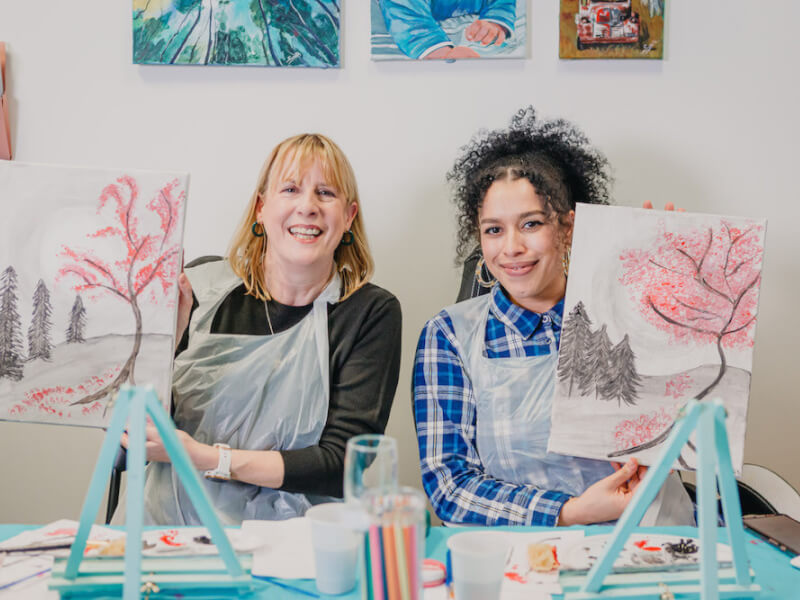 Two women hold up their paintings